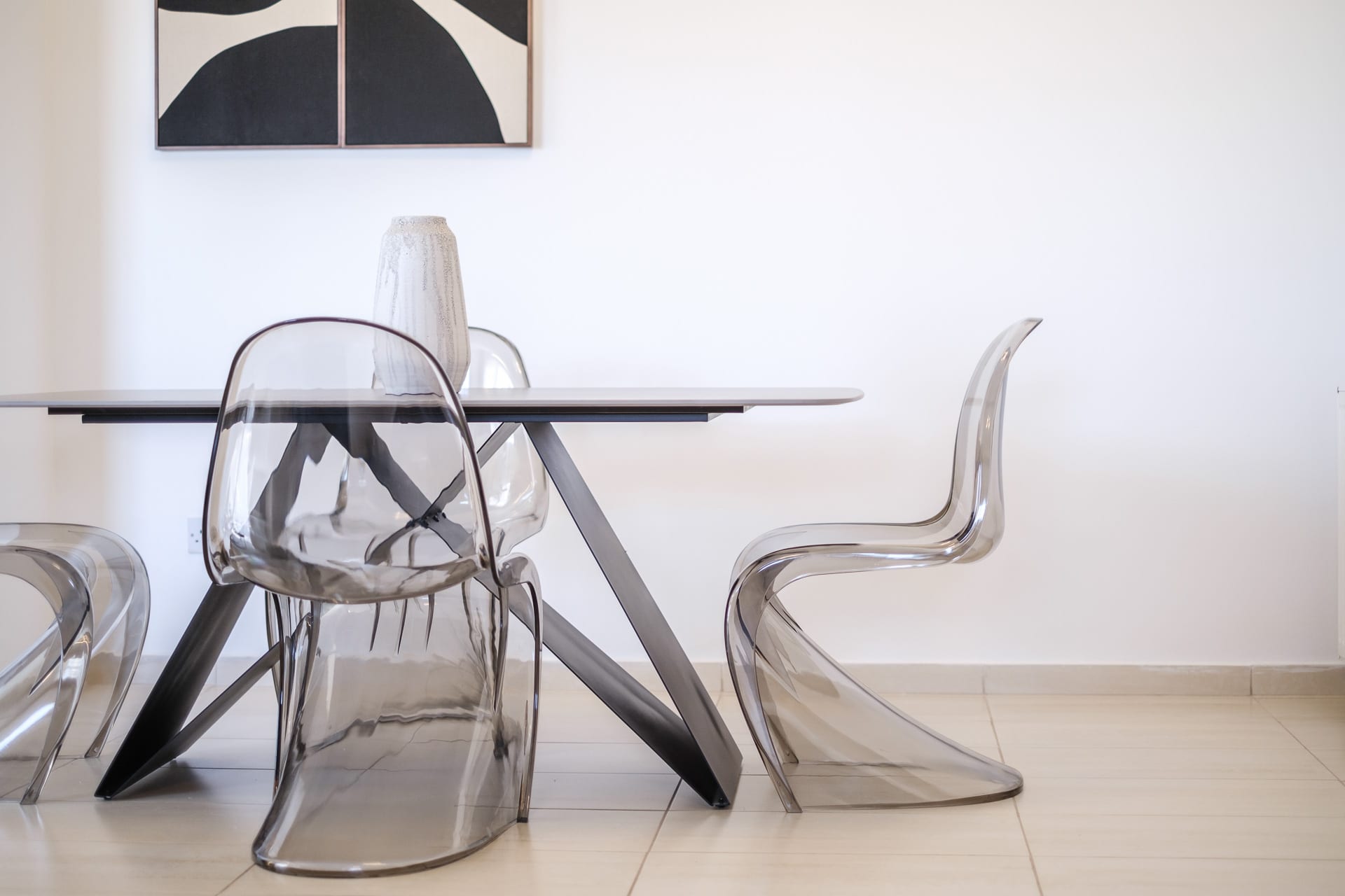 Dining table with transparent acrylic chairs beneath black-and-white abstract artwork