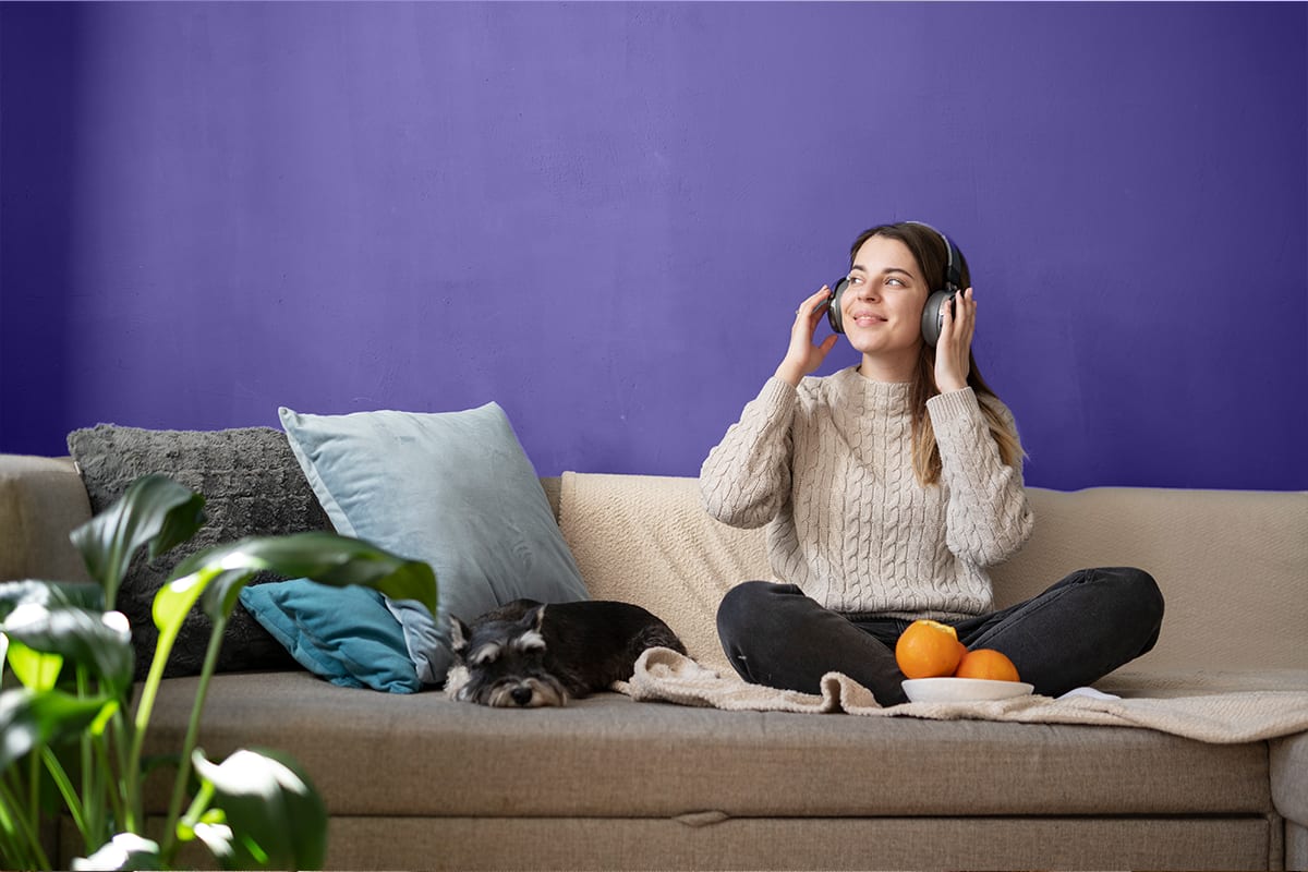 Woman with headphones relaxing cross-legged on a sofa next to a sleeping dog