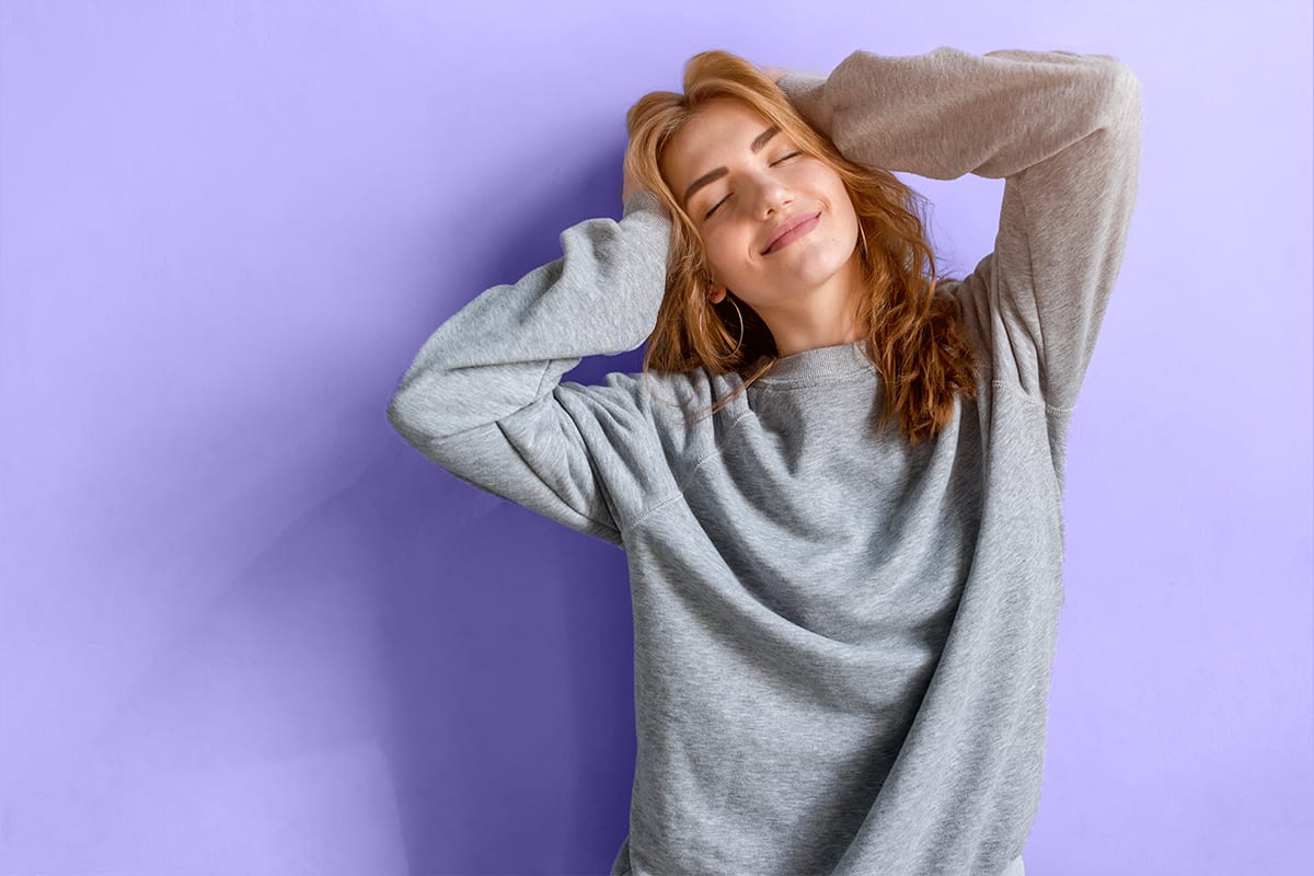 Relaxed woman in a grey sweater stretching with her eyes closed