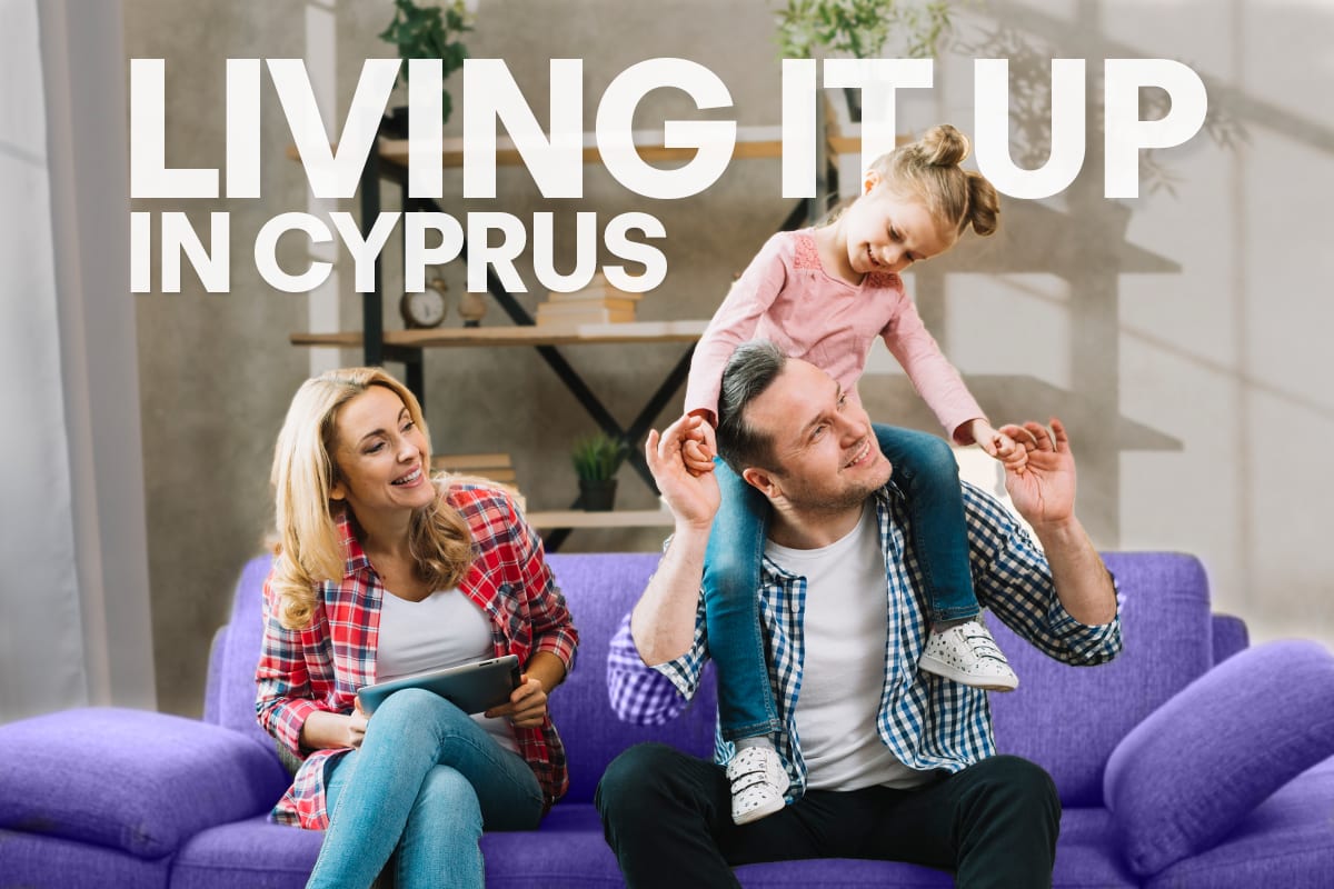 Family relaxing on a purple sofa, a child on a parent’s shoulders, under the words “Living it up in Cyprus”