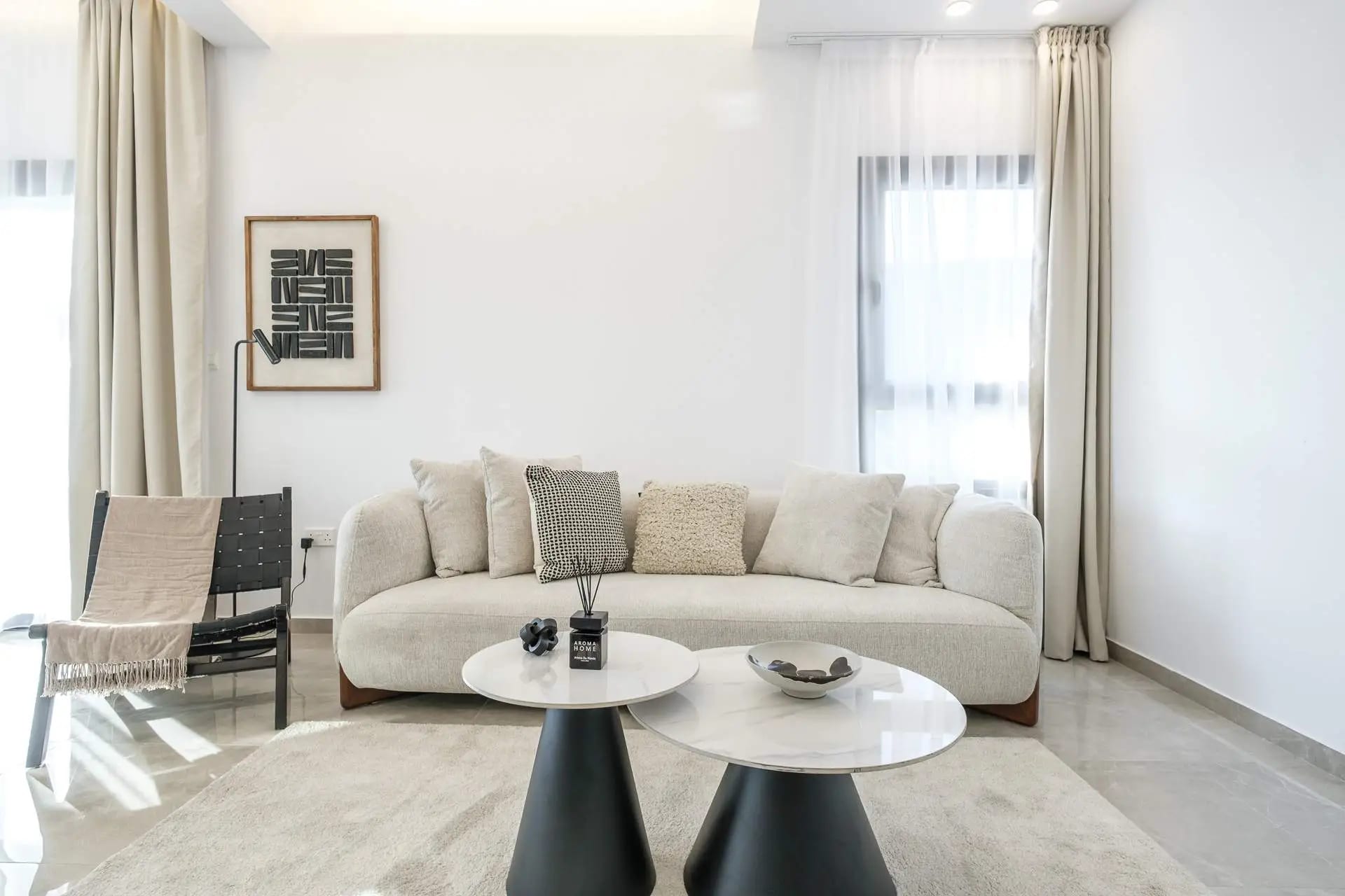 Bright living room with a curved cream sofa, round marble coffee tables and sheer curtains