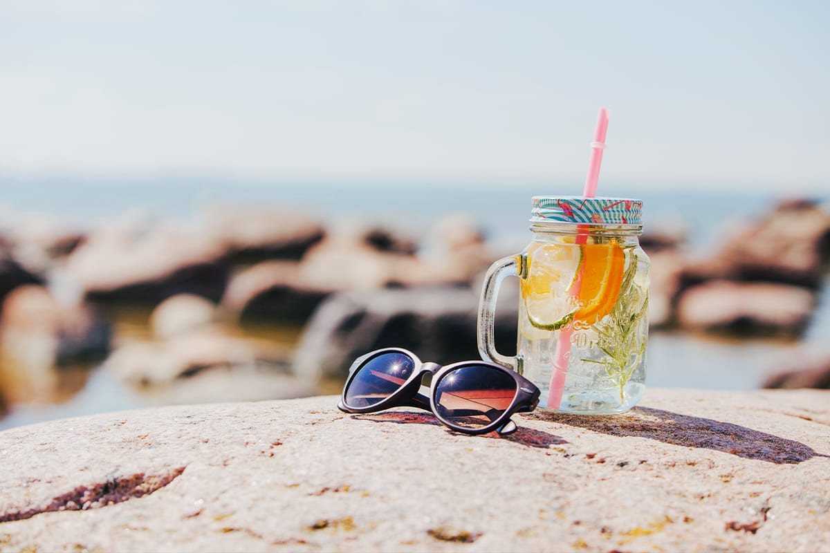 Sunglasses and a glass of citrus iced drink on a seaside rock
