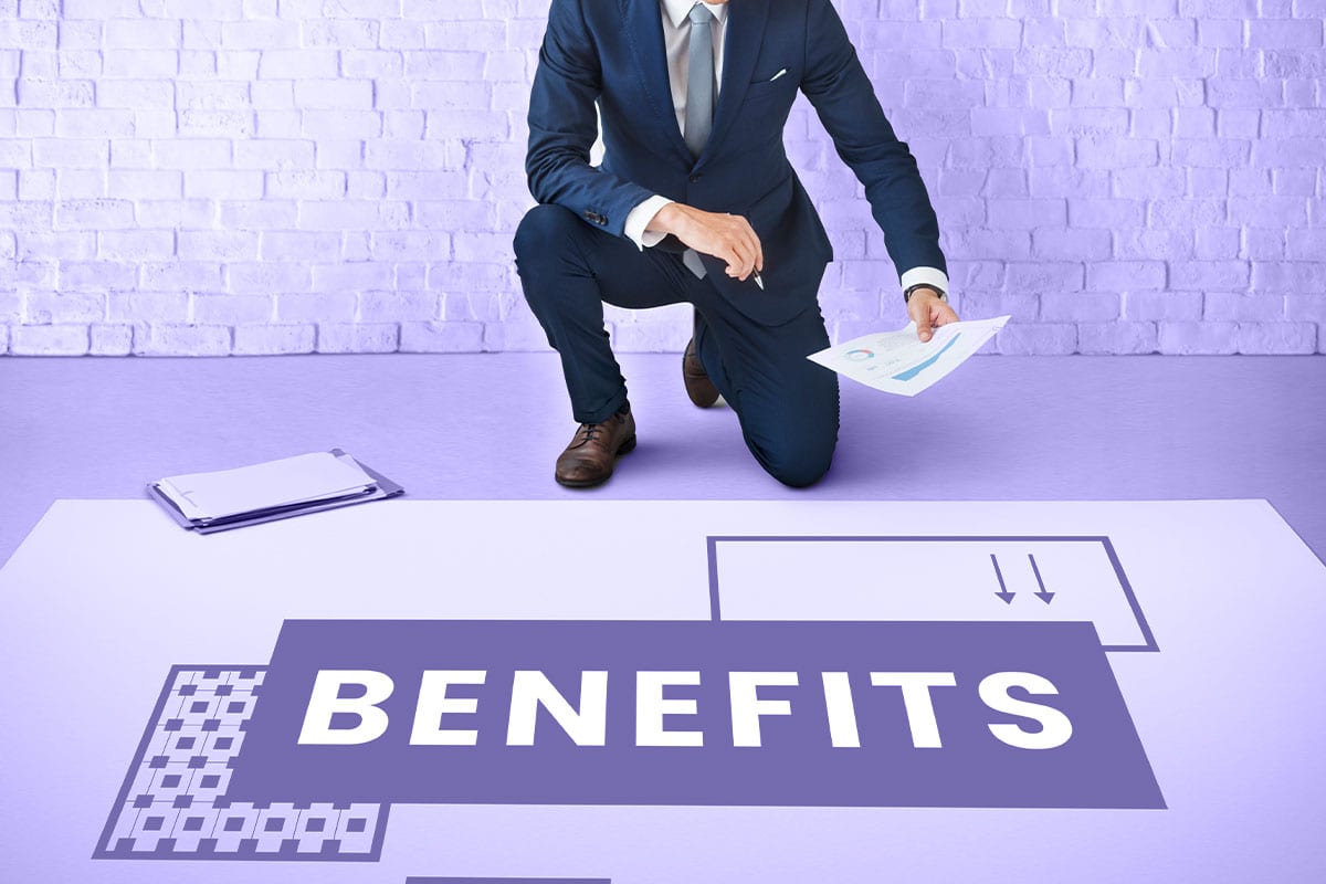 Businessman kneeling over a floor plan marked “Benefits”