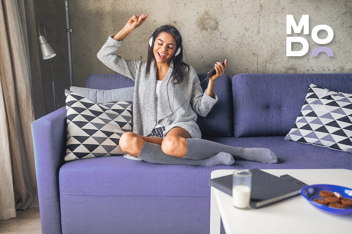 Woman with headphones dancing on a sofa in a living room