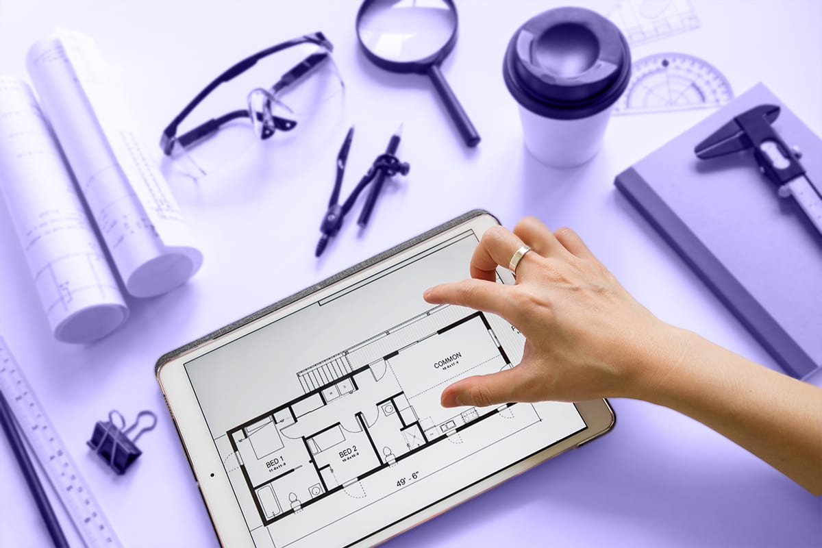 Hand zooming into an apartment floor plan on a tablet, surrounded by drafting tools