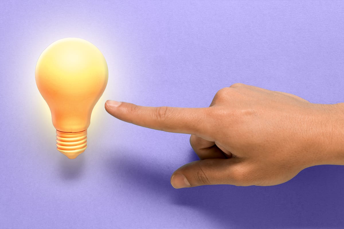 Finger pointing at a glowing light bulb on a purple background