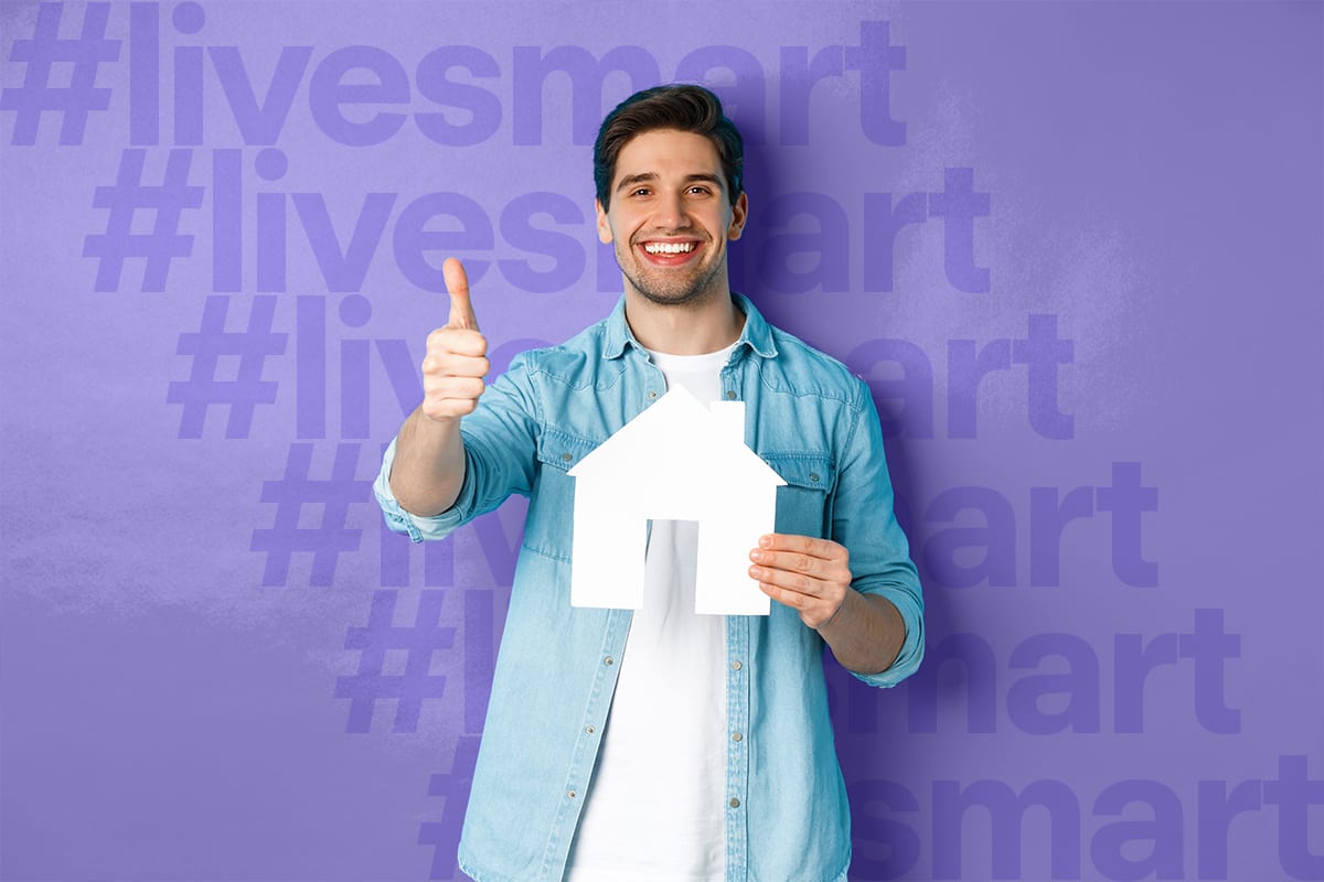 Smiling man giving a thumbs-up and holding a paper house cut-out in front of “#livesmart” lettering